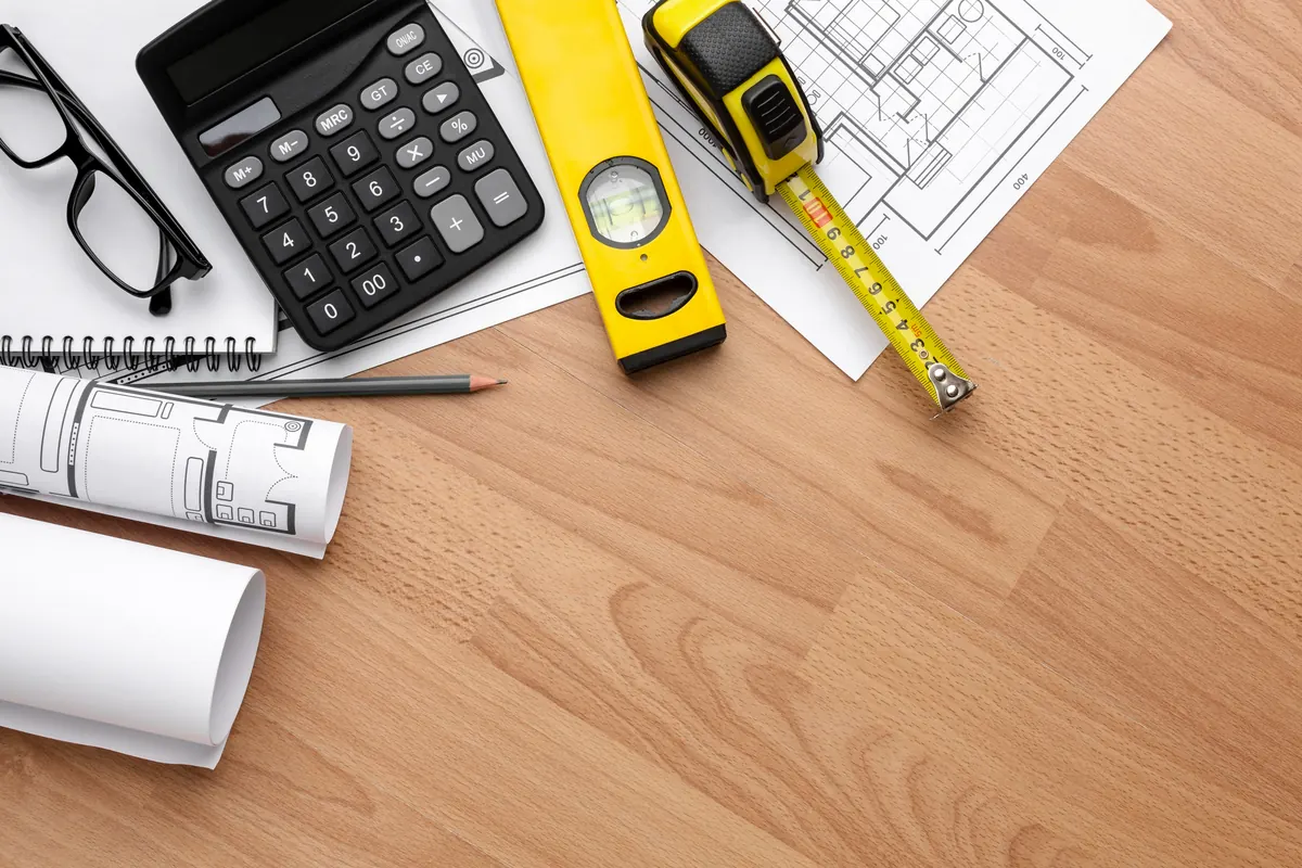 Calculator, tape measure, level and floor plans on a wood floor