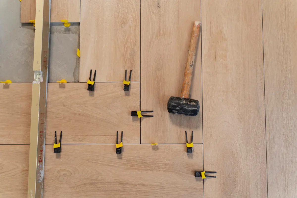 Tile leveling clips and a rubber mallet on a wood-look porcelain tile floor during installation