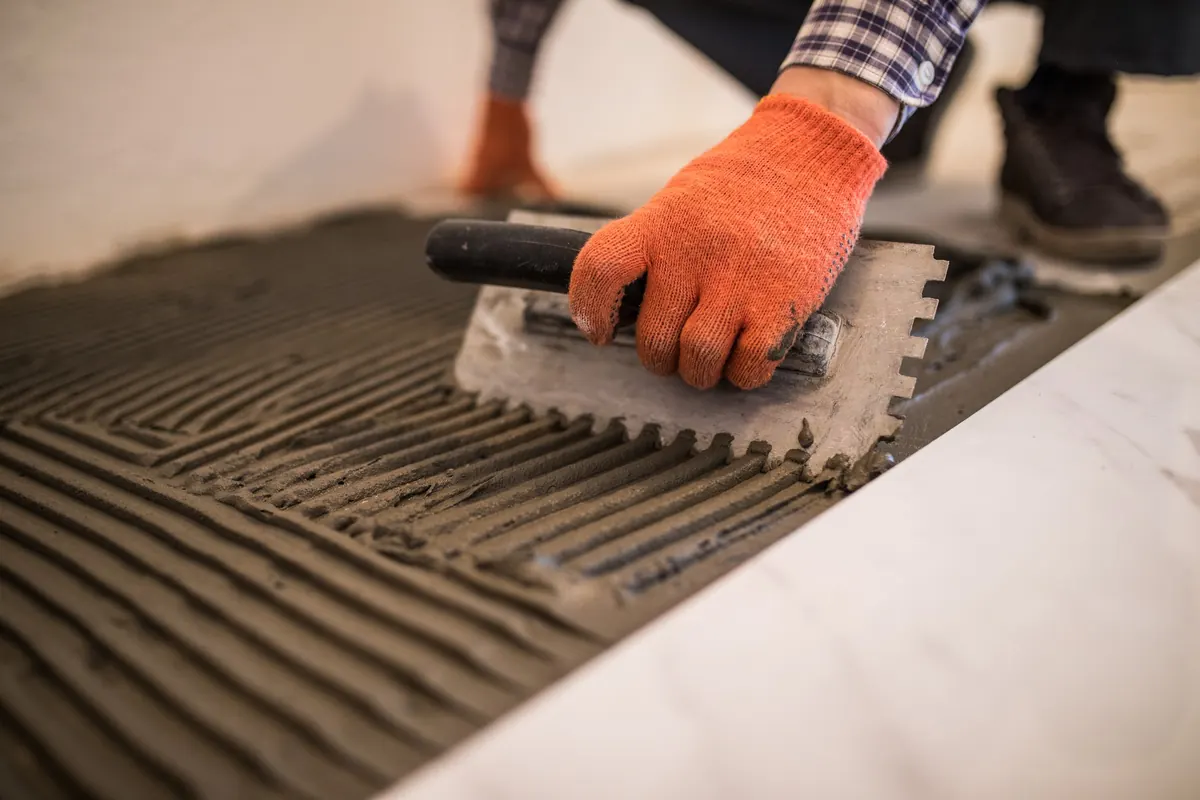 Troweling mortar onto a concrete floor before laying tile