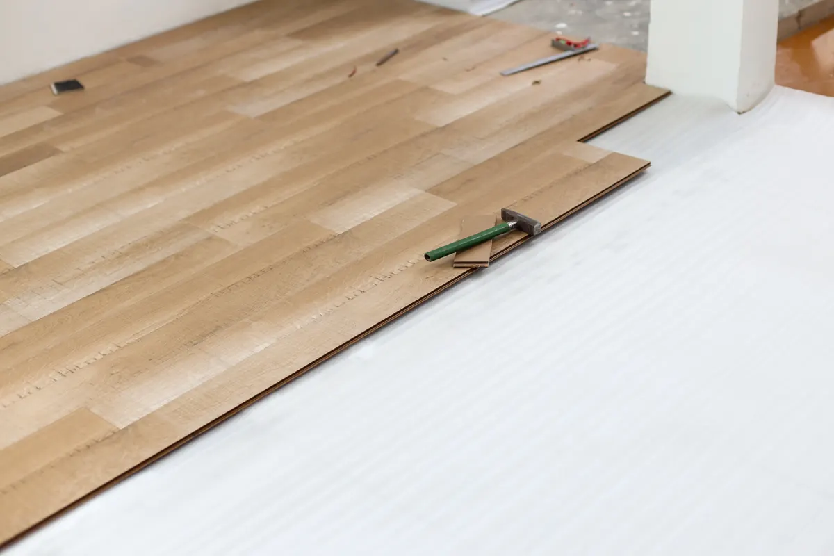 Light oak-look floating floor being laid over white foam underlayment